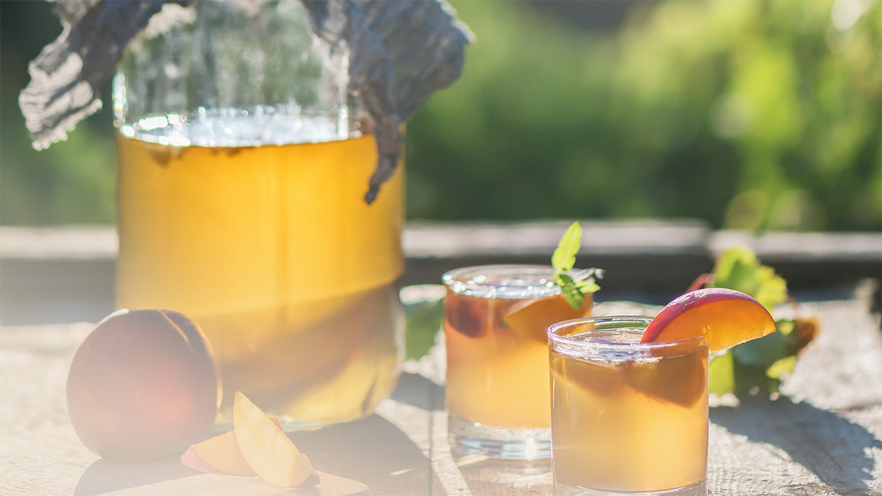 Kombucha Pfirsich Eistee  Glasbehaelter zwei Glaeser Pfirsiche draussen Abendsonne